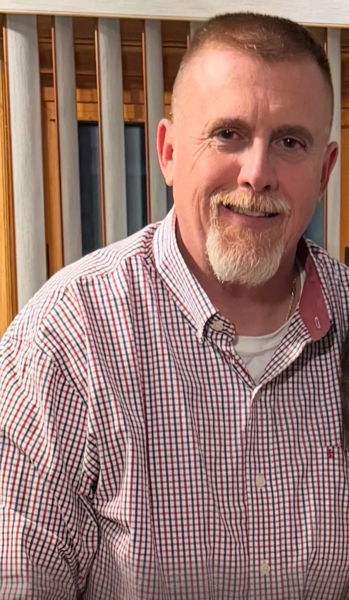 A man with a beard and mustache wearing a red checkered shirt.
