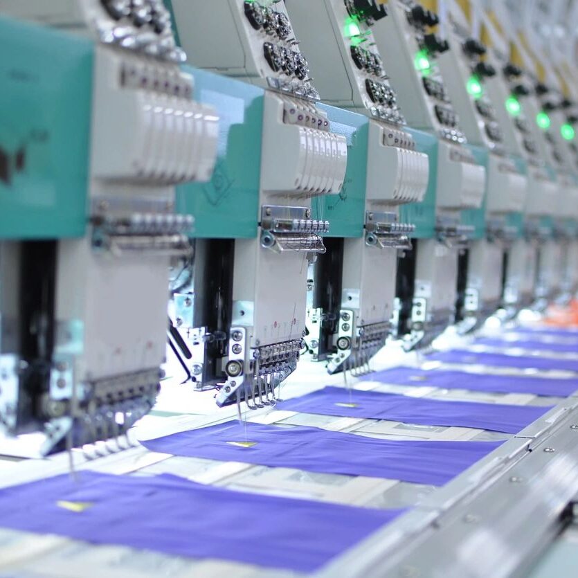 fm=f_GpK8Kel A row of machines in a factory with blue fabric on the sewing machine.